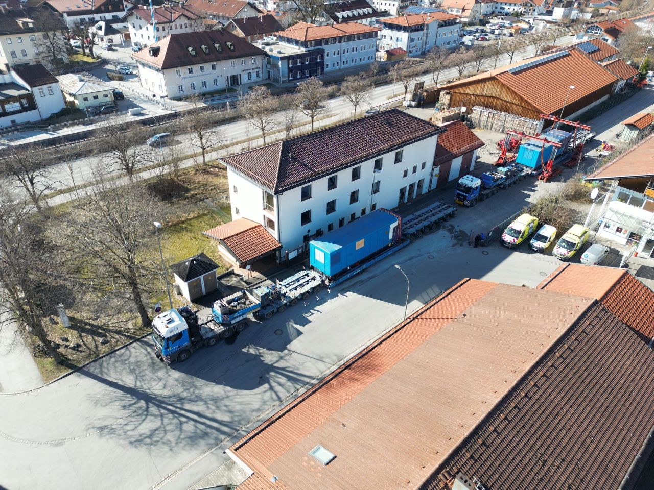 Large blue generator on a multi-axle heavy transport trailer being hauled through a small town street.