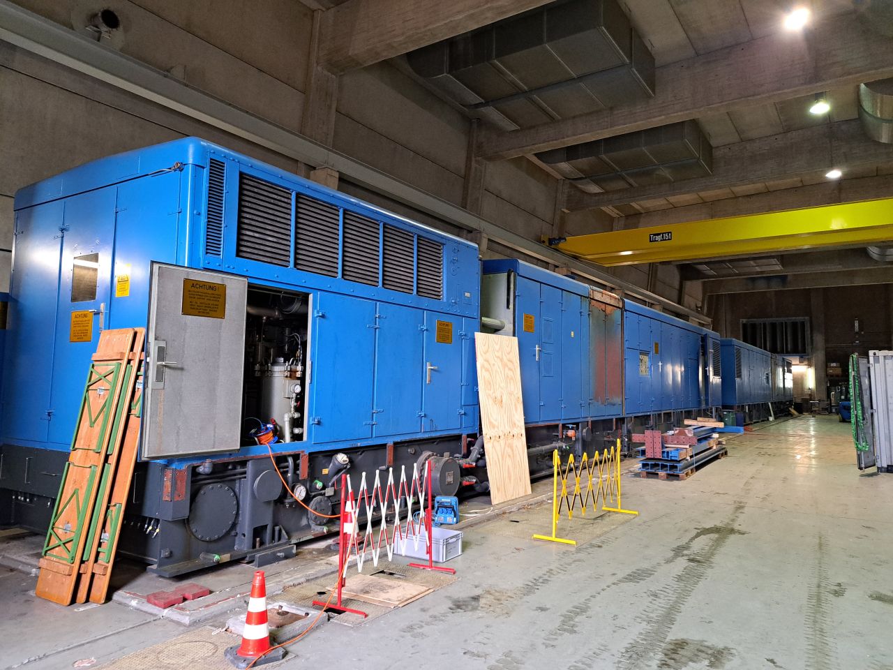 Large blue generator modules inside the Hausham power plant hall with safety barriers and maintenance equipment.