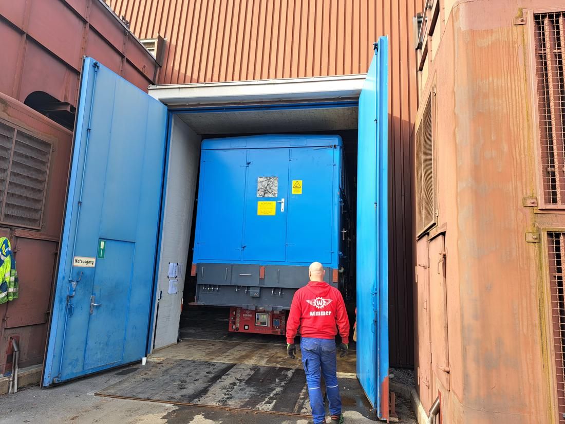 Large blue generator being moved out of the Hausham power plant through wide blue doors.