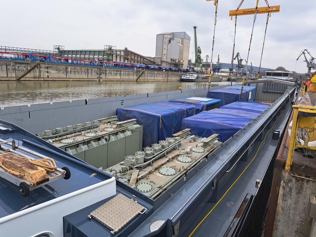 Large generator units and equipment secured on a barge deck alongside a river quay.