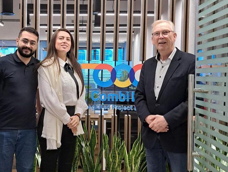 Three people standing in front of the Combi Lift MEA office entrance, smiling for the camera.